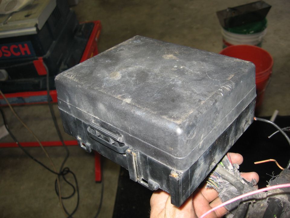 Dusty black fuse box with wires held by a hand, Bosch tool in background