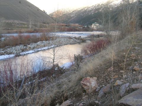1996 Ford Bronco - A wide river flows through a valley with mountains in the background. The banks of the river are lined with rocks and bare trees.