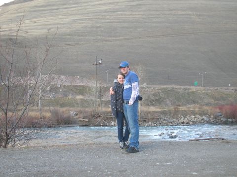 1996 Ford Bronco - A couple stands arm-in-arm by a river with a large, barren hill in the background.
