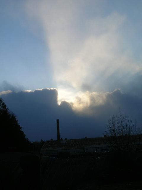 1996 Ford Bronco - A dark, cloudy sky with sunbeams breaking through the clouds over a silhouetted industrial building with a tall smokestack.