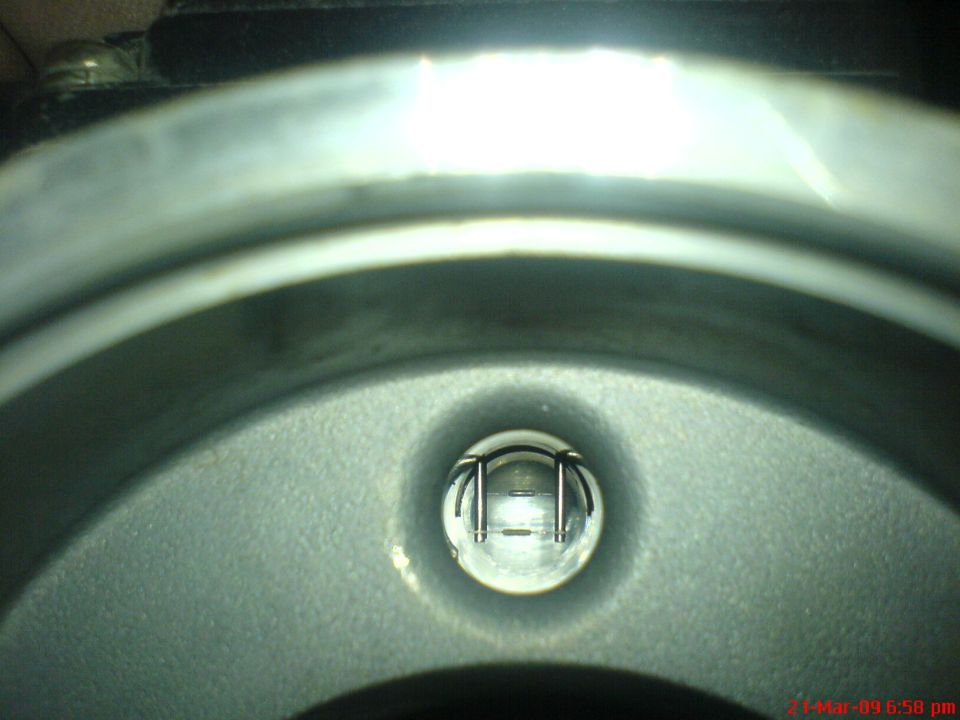 Close-up of a metallic component with a central glass lens showing internal structure.