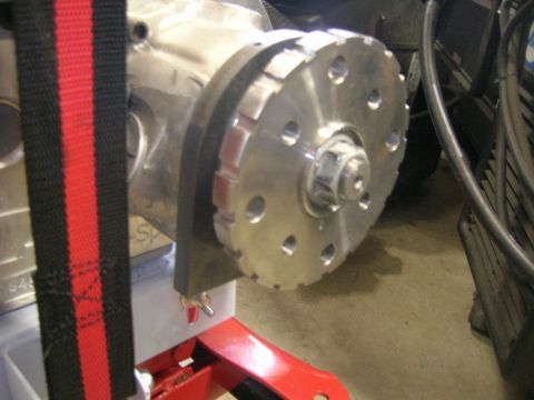 1996 Ford Bronco - A close-up view of a silver metal pulley with multiple bolt holes and a black and red strap in the foreground, attached to a vehicle's engi…