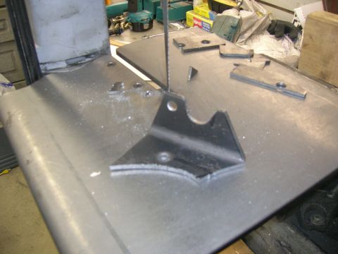 1996 Ford Bronco - A metal bracket is being cut on a band saw with metal shavings scattered across the table. Several other metal pieces and tools are visible…