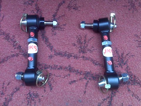 2008 Jeep Wrangler - Two black adjustable control arms with white 'JKS' stickers and red adjustment screws are laid out on a red textured surface.