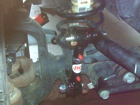 2008 Jeep Wrangler - A close-up, low-angle shot of the suspension system of a Jeep Wrangler JK, showing a black adjustable control arm with red accents and "JK"…