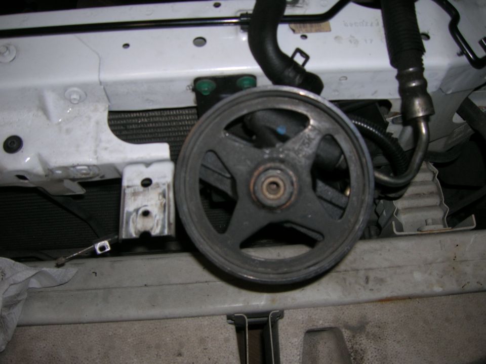 Dark five-spoke serpentine pulley resting near a white radiator support with hoses