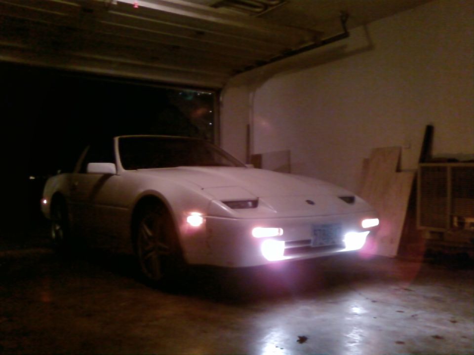 White convertible sports car with headlights on in a garage.