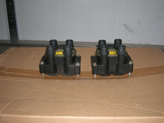 Two black ignition coil packs with yellow labels on cardboard