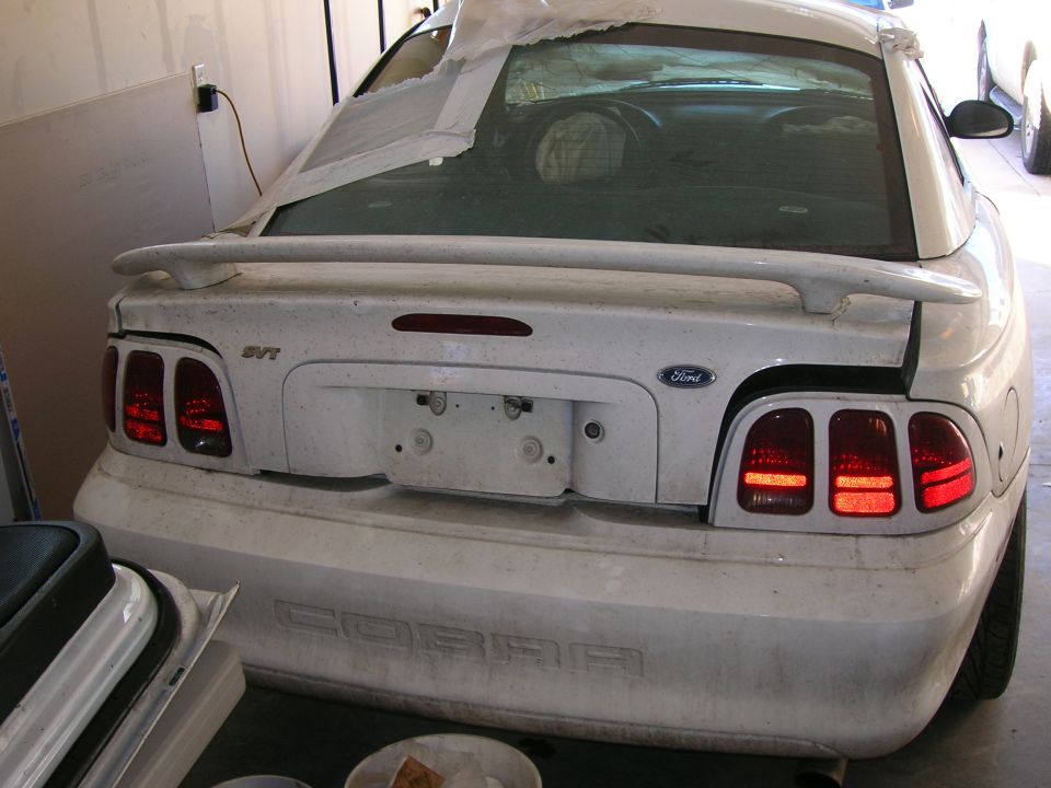 Rear view of a dusty white 1998 Ford Mustang SVT Cobra with spoiler and original taillights.