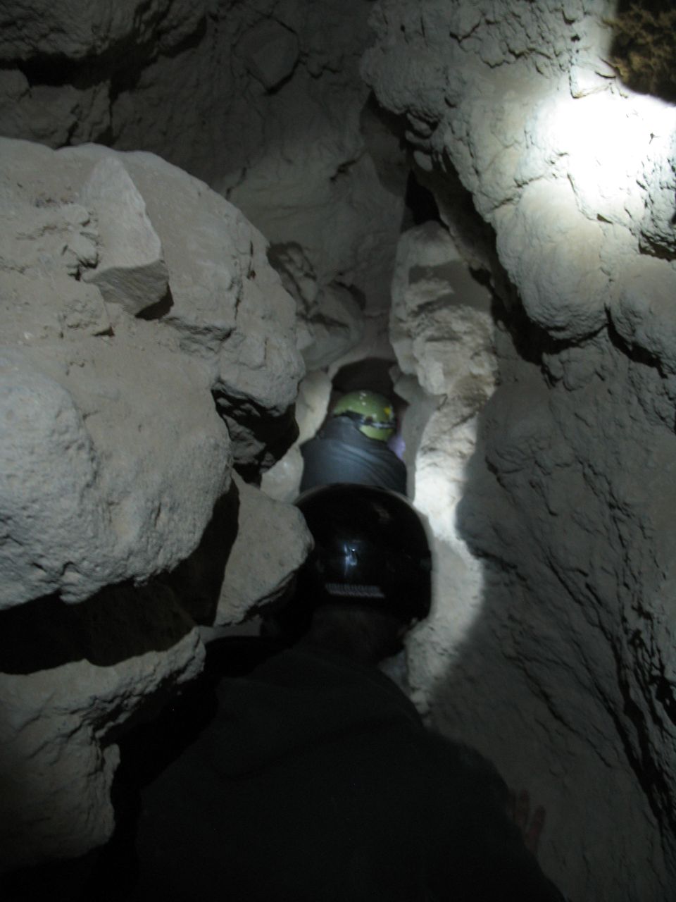 Two people in helmets exploring a narrow cave passage.