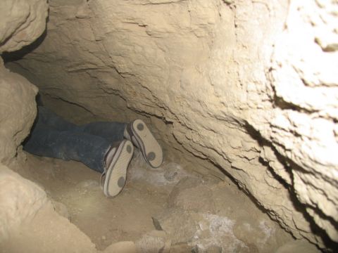 1984 Ford Bronco - A person's legs and feet are visible as they lie down in a narrow cave or tunnel. The person is wearing blue jeans and casual shoes.