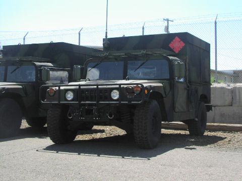 1981 Ford Bronco - Two olive drab Humvees are parked outdoors, one with a camouflaged cargo box and a red diamond marker.