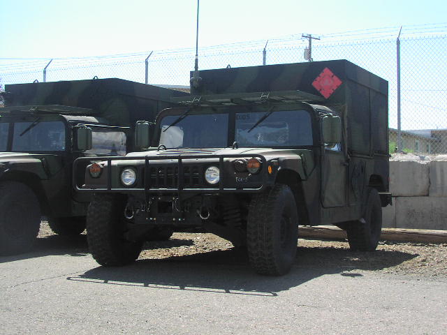 Green Humvee with camouflage cargo box and red diamond marker, parked next to another Humvee