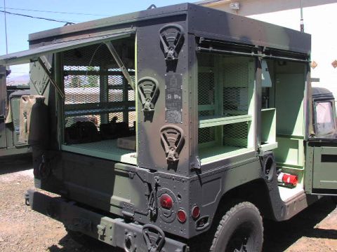 1981 Ford Bronco - A military truck with a cage-like cargo area is shown from the rear with its doors open, revealing shelving inside.