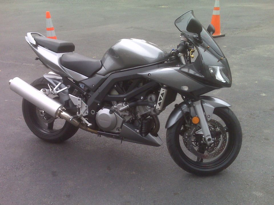 Silver sport motorcycle parked on asphalt with orange traffic cones.