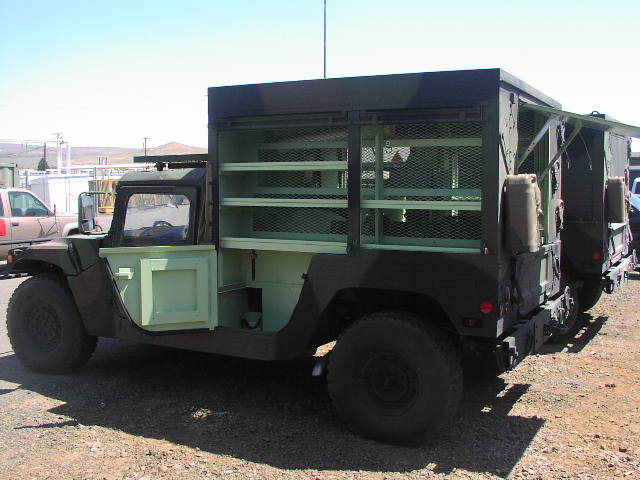 Military truck with open side doors revealing storage shelves and mesh cages