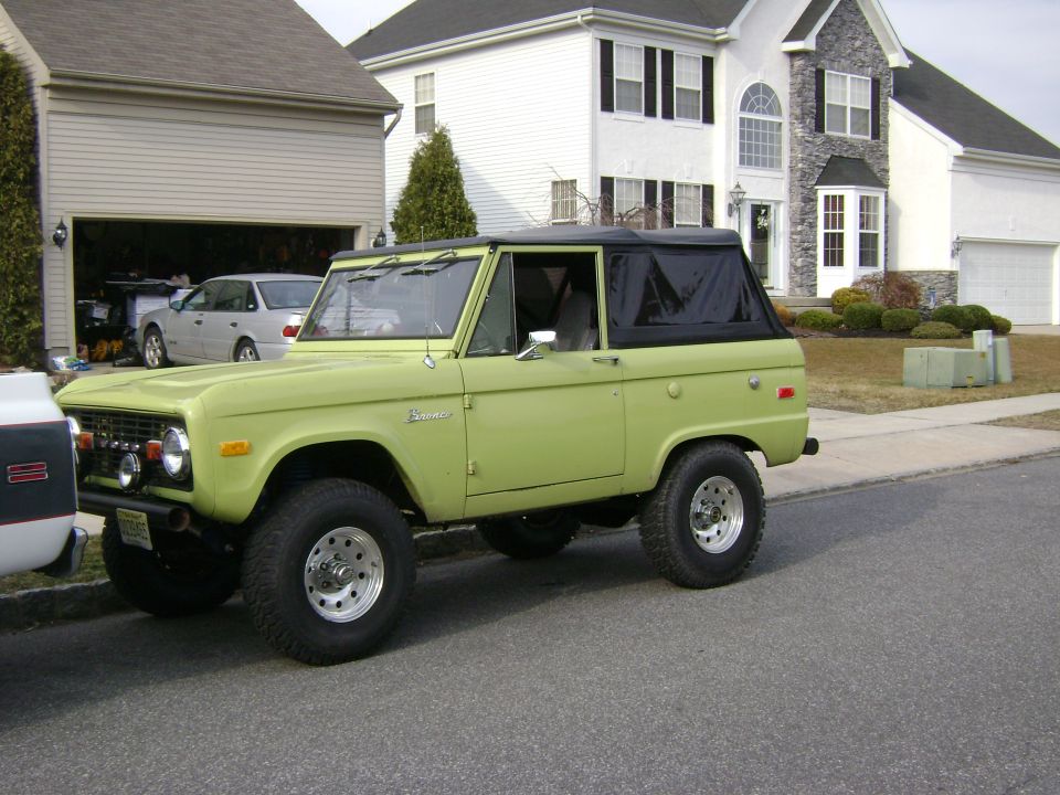 Lime green 1974 Ford Bronco with a black soft top, parked on a residential street