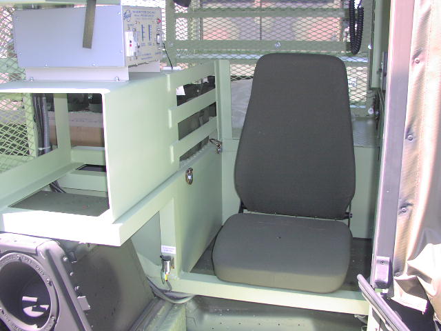 Interior of a military vehicle showing a seat, equipment rack, and speaker