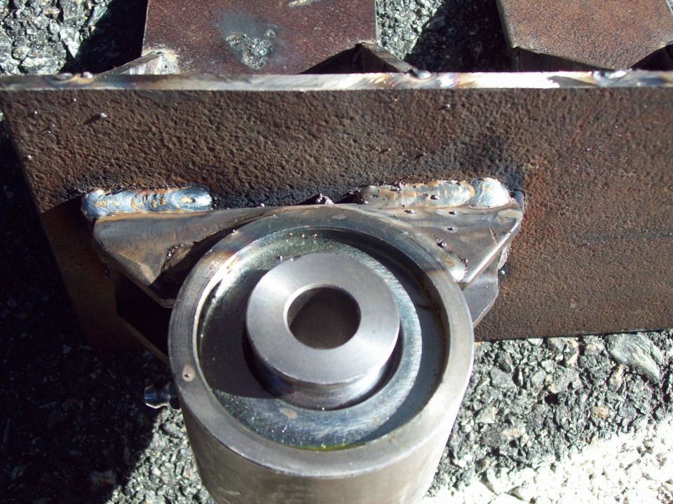 Close-up of a welded metal bracket attached to a cylindrical part, with visible weld marks and a metal bushing