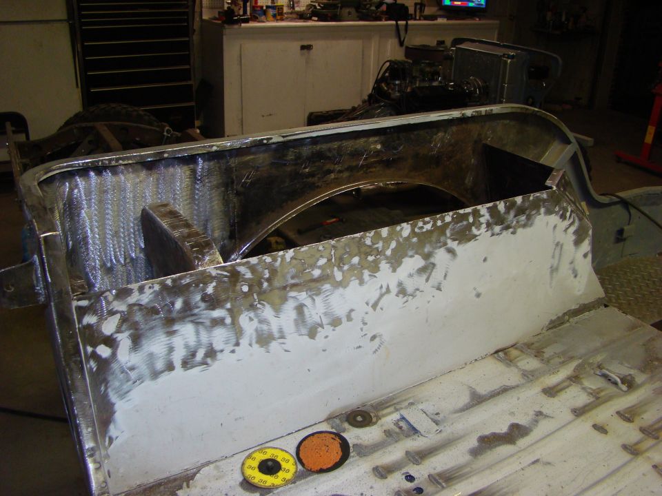 Vehicle body section with visible welding and body filler, showing interior wheel well. Two sanding discs are on the floor