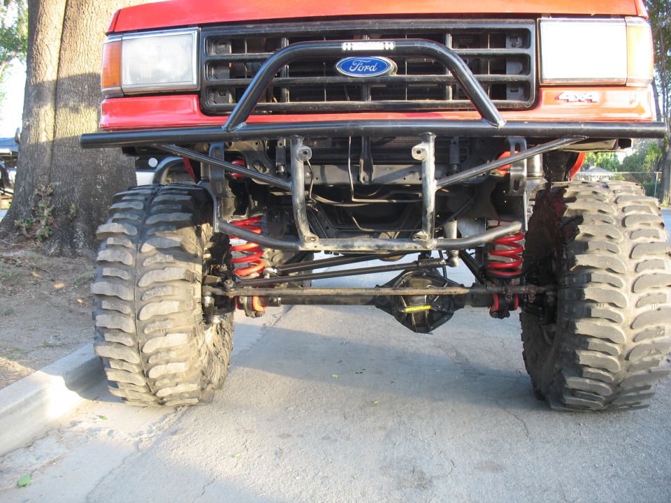 Front view of lifted red Ford 4x4 showing tube bumper, red coils and Dynatrac front diff
