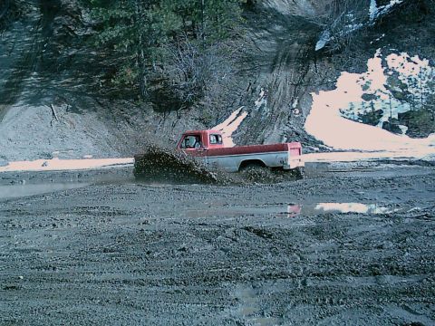 1968 Ford F-250 - A two-tone pickup truck navigates a muddy terrain, kicking up a significant spray.