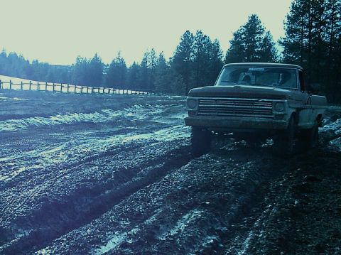 1968 Ford F-250 - A Ford F-Series truck navigates a challenging muddy terrain, with trees and a wooden fence visible.
