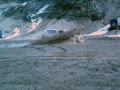 1989 Ford Bronco - A 1989 Ford Bronco navigates a muddy off-road course, kicking up a large spray of water and mud.