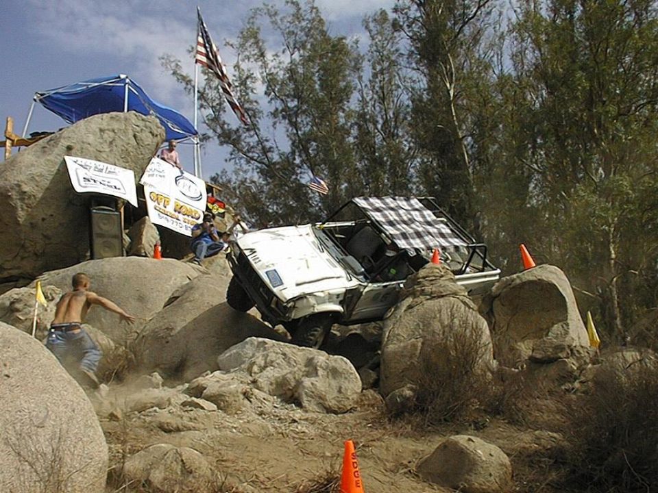 White off-road vehicle climbing large rocks with checkered roof