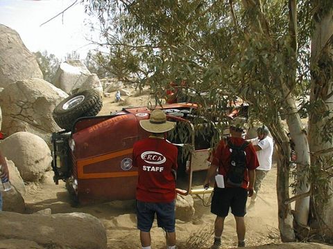 1997 Ford Ranger - An off-road vehicle has overturned on a rocky trail, with onlookers present.