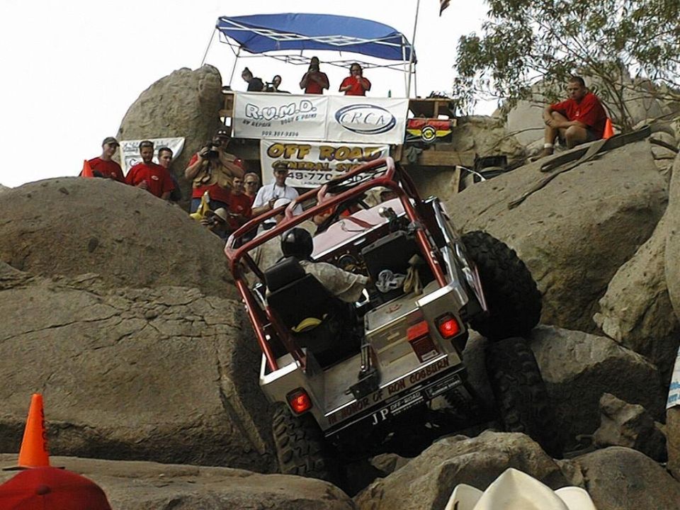 Off-road buggy with red roll cage climbing rocky terrain, rear view