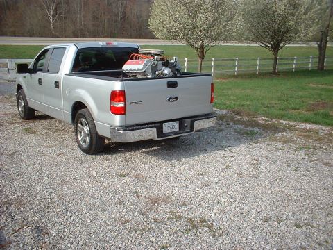 1970 Ford Mustang - A silver Ford F-150 pickup truck is parked on a gravel surface, with a V8 engine loaded in its bed.