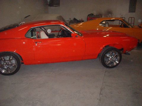 1970 Ford Mustang - A red 1970 Ford Mustang coupe is parked next to an orange coupe in a garage.