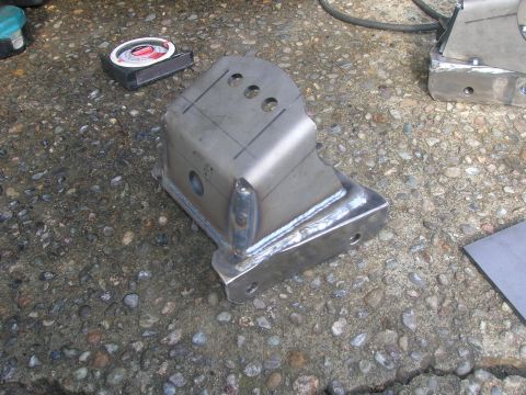 1996 Ford Bronco - A custom metal bracket, likely for vehicle suspension, sits on a gravel surface next to a tape measure.