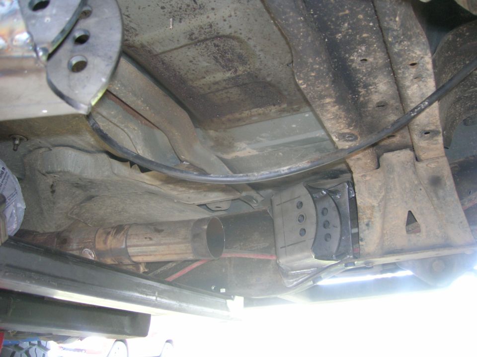 Underside of vehicle with exhaust pipe and suspension components, showing metal brackets and rust