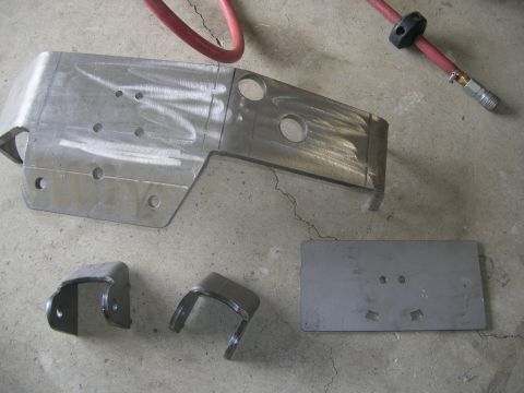 1996 Ford Bronco - Unidentified fabricated metal parts, possibly for vehicle suspension, laid out on a concrete surface.