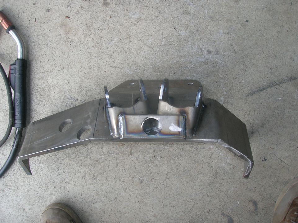 Custom steel suspension bracket with welded joints and cutouts on concrete floor.