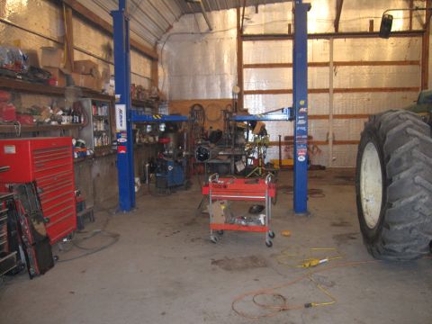 1992 Ford Bronco - A vehicle is elevated on a lift inside a garage, with a red tool chest and a large tire visible nearby.