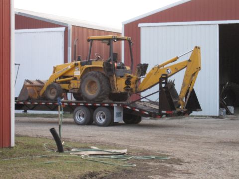 1992 Ford Bronco - A yellow backhoe loader is parked on dirt between two buildings.