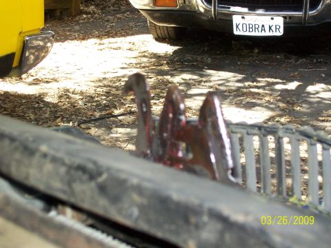 1973 Mercury Cougar - A close-up view of a vehicle's hood latch mechanism, with another vehicle's license plate visible in the background.
