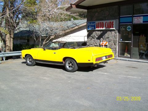 1973 Mercury Cougar - A yellow 1973 Mercury Cougar convertible is parked in front of Cedar Glen Auto Care.