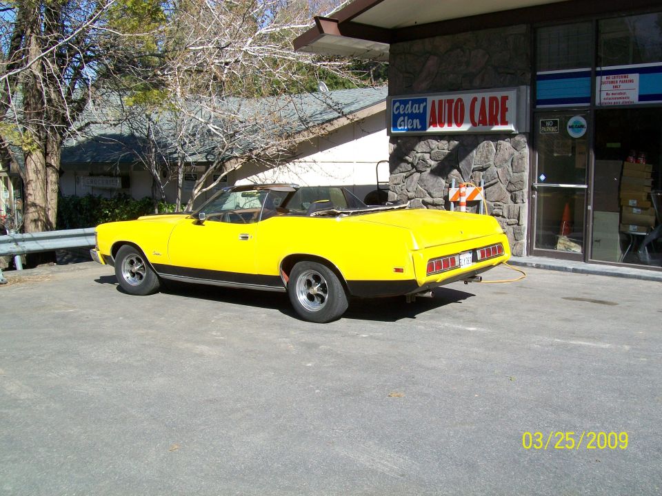 yellow 1973 Mercury Cougar convertible parked outside auto repair shop