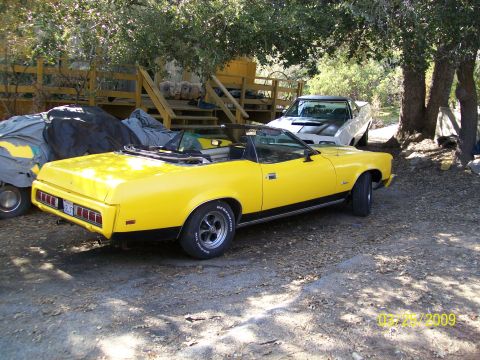 1973 Mercury Cougar - A yellow 1973 Mercury Cougar convertible is parked next to another vehicle.