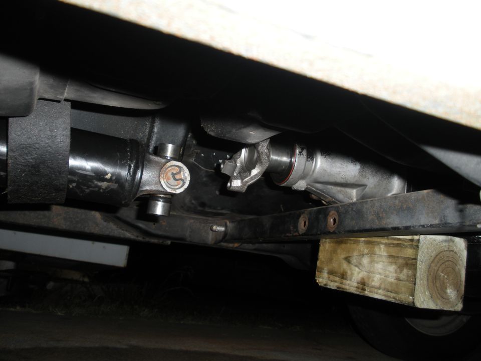 Underside view of a vehicle's driveshaft connected to a differential, supported by wooden blocks