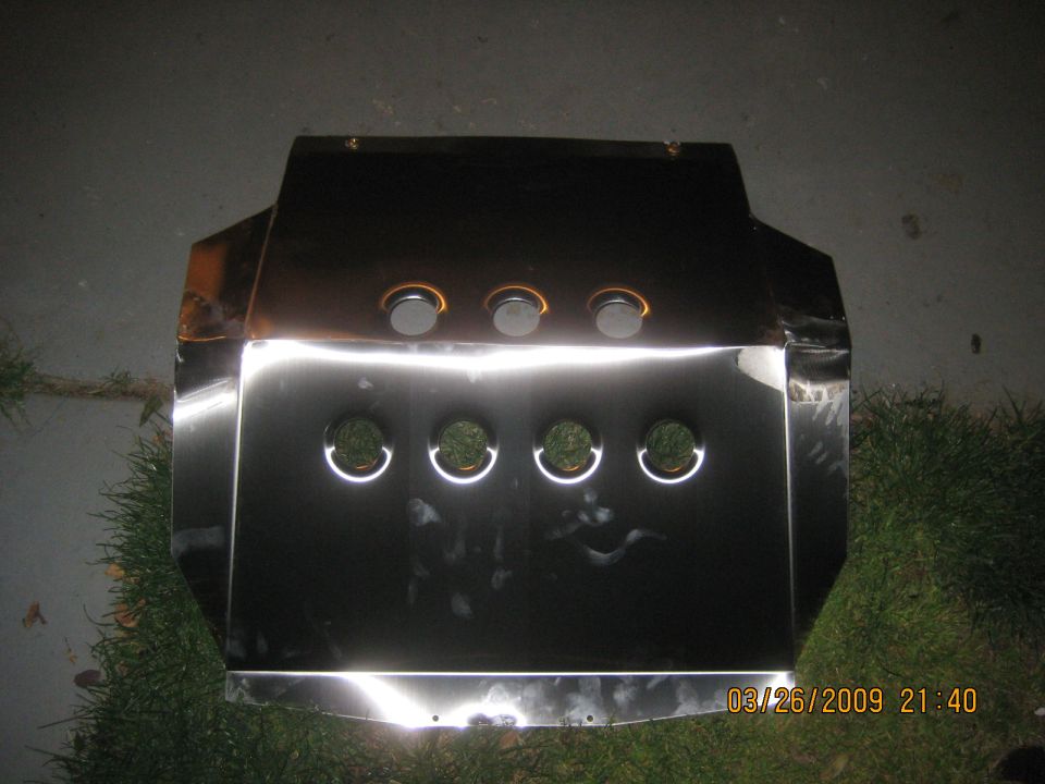Polished metal skid plate with drilled lightening holes lying on grass