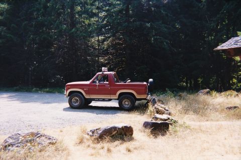 1985 Ford Bronco - Side view of a red and tan 1985 Ford Bronco parked outdoors.
