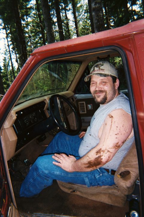 1985 Ford Bronco - A man sits in the interior of a red truck, his arms and shirt covered in mud.