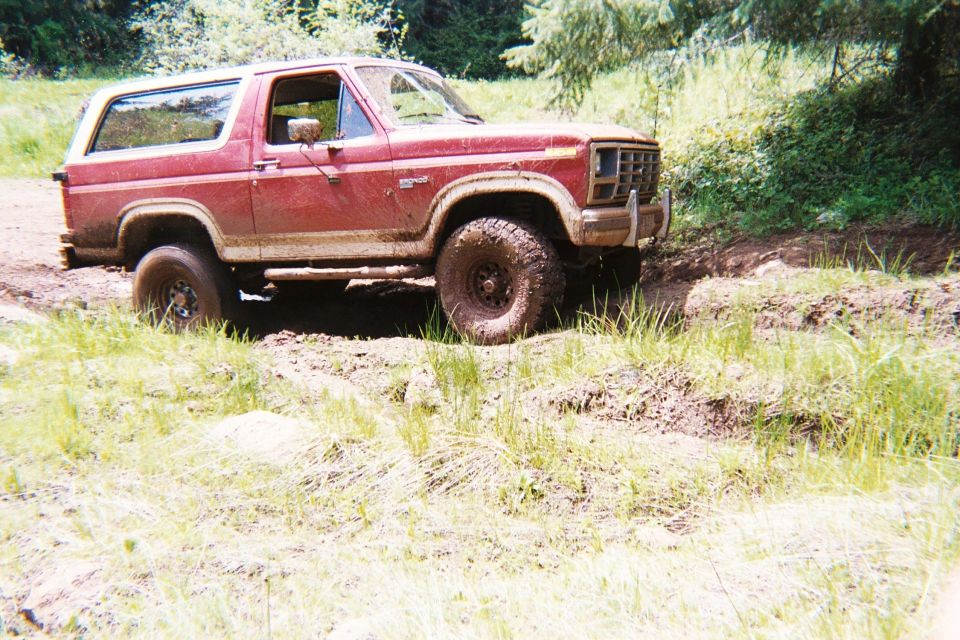 Red Ford Bronco with a white top driving off-road