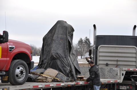 1996 Ford Bronco - A tarp-covered object is being transported on a flatbed truck, alongside a red pickup truck.