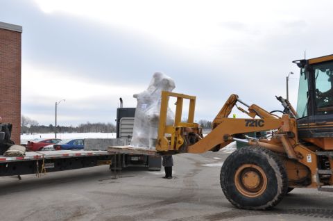 1996 Ford Bronco - A loader is used to move a large piece of equipment wrapped in plastic from a flatbed trailer.